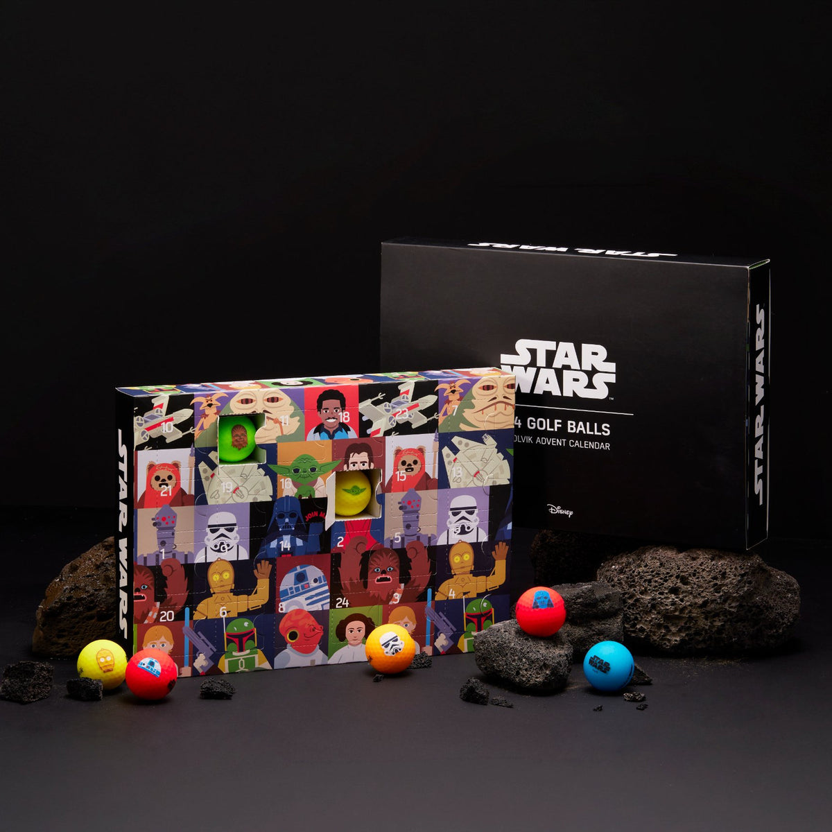 Star Wars golf ball advent calendar displayed with its black branded box, a colorful character collage tin, and several golf balls on a dark studio background with rocks.